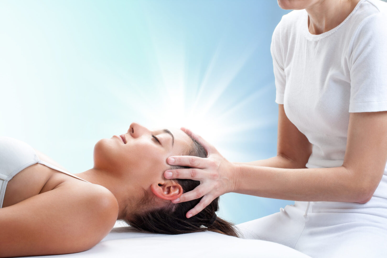 Close up portrait of therapist doing healing treatment on young woman.Therapist touching head with light glow in background.